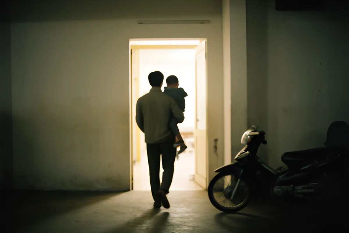 Một người đàn ông bế theo một đứa trẻ nhỏ, cả hai quay lưng bước nhanh về phía cửa sáng đèn của một tòa nhà