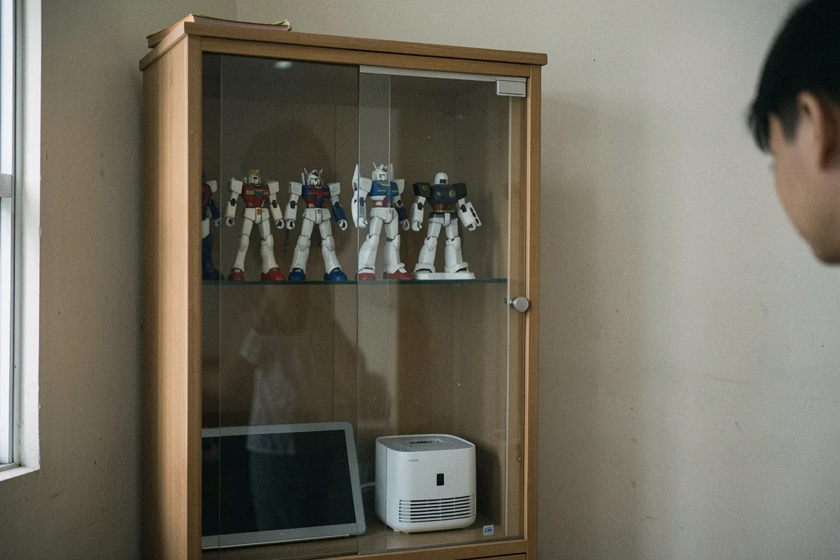 Tủ kính gỗ chứa các mô hình robot và một hộp trắng, đầu một người hiện ở mép phải, ánh sáng dịu