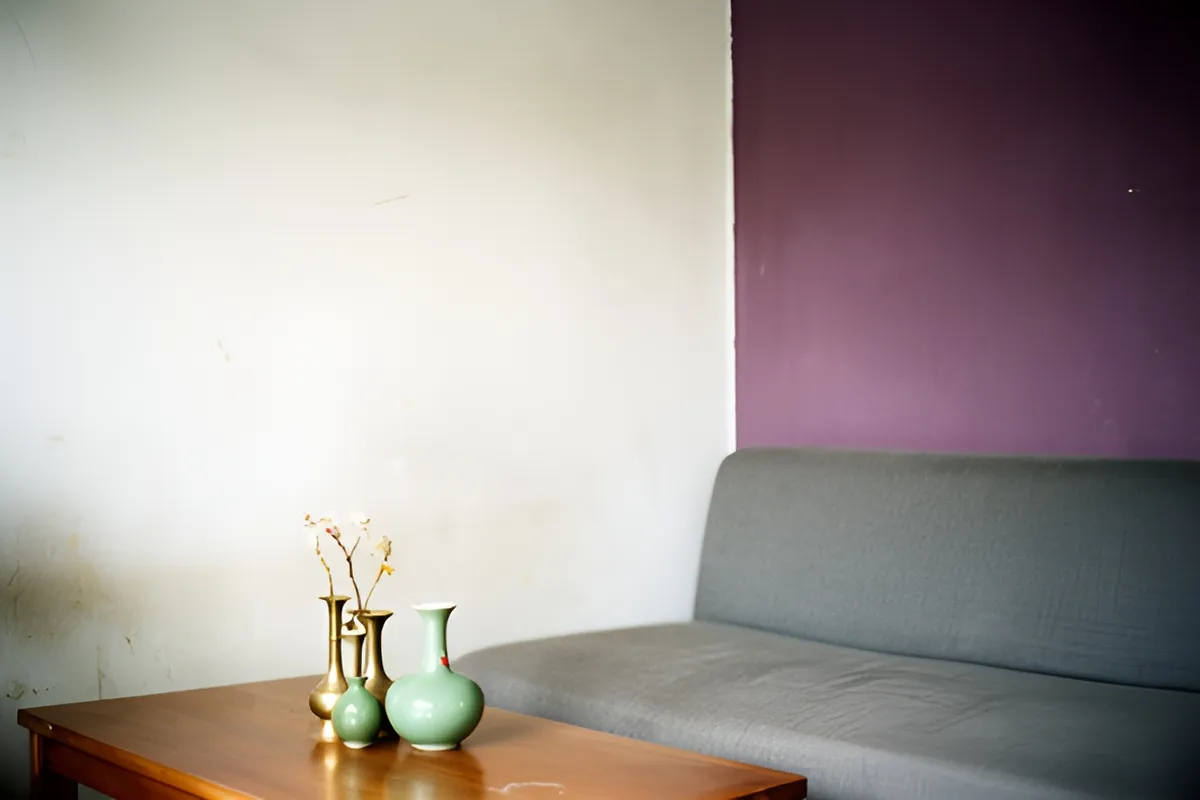 Phòng khách không người với ghế sofa xám, tường tím đậm và các bình gốm xanh, đồng đặt trên bàn gỗ, ánh sáng ban ngày dịu